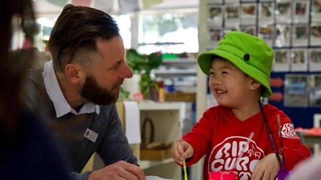 A teacher speaks to a kindergarten-aged student who is painting a picture