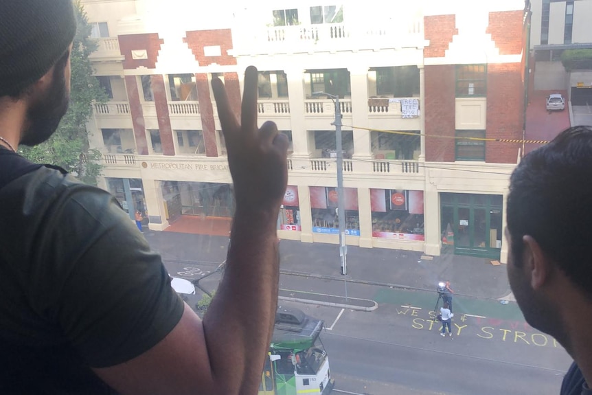 Two men stand at a window looking down at the street.