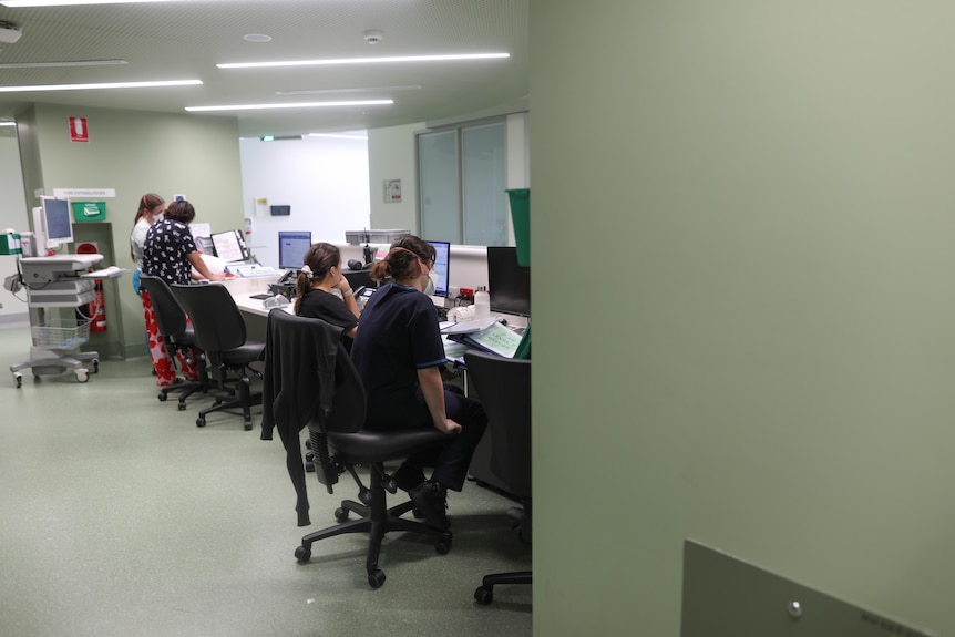 In a staffroom with pale green walls, four midwives look over paperwork.