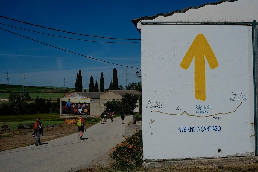 Ein gelbes Schild an einer Mauer weist Wanderer, die den Camino pilgern, in die richtige Richtung 