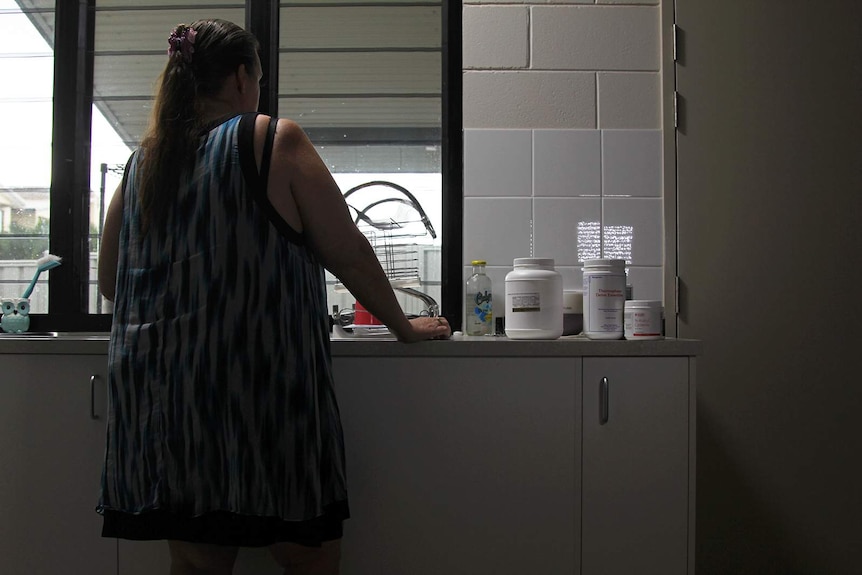 A photo of public housing tenant Annalee Small leaning on a kitchen counter, with medication visible beside her.