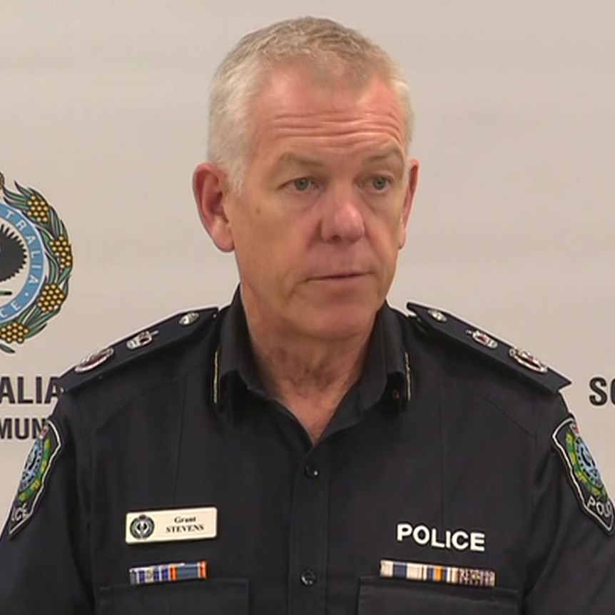 A man in police uniform in front of a wall with police logos on it