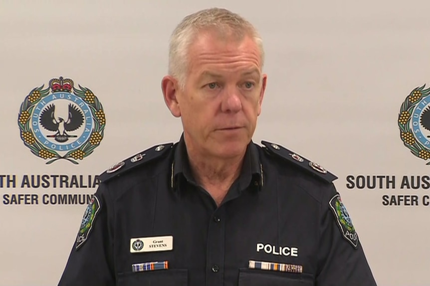 A man in police uniform in front of a wall with police logos on it