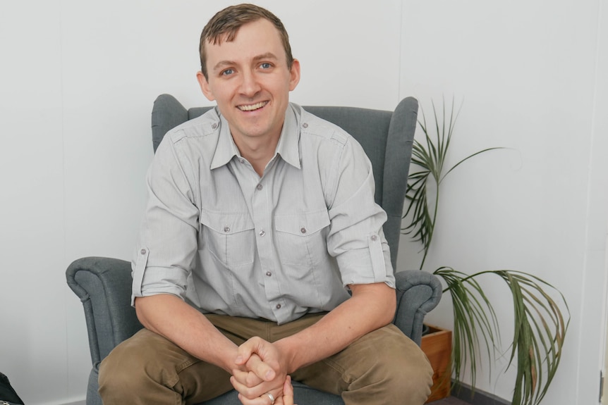 A man sits on a coach smiling.