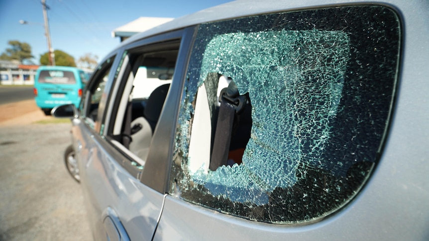 A close up of a silver car with its windows smashed.