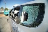 A close up of a silver car with its windows smashed.