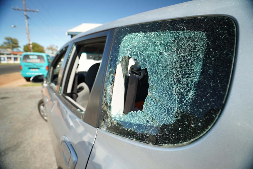 A close up of a silver car with its windows smashed.