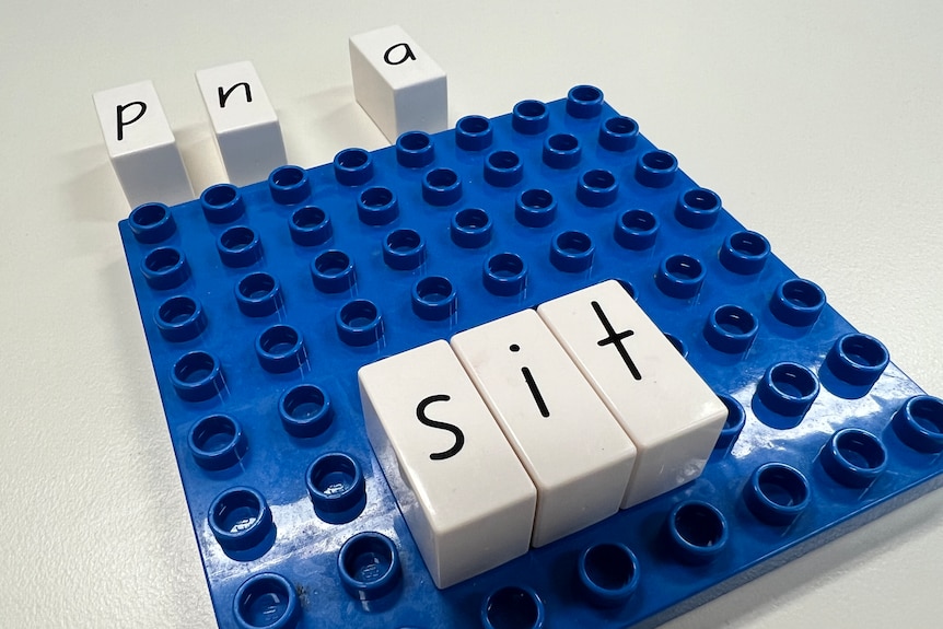 A blue block board with alphabet blocks on top spelling the word 'sit'. 