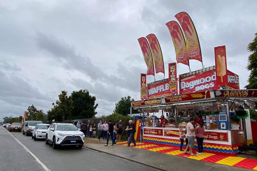 A food stall selling dagwood dogs and other show foods operates on the side.