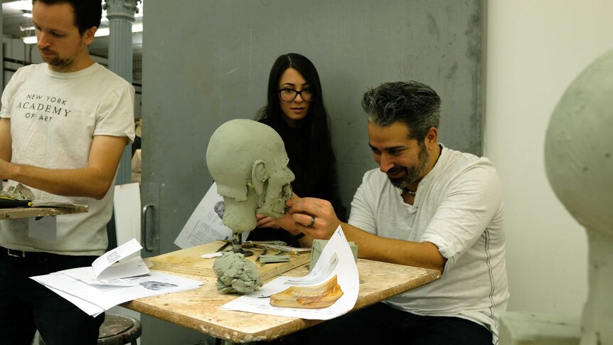 A teacher shows an art student how to sculpt a face.