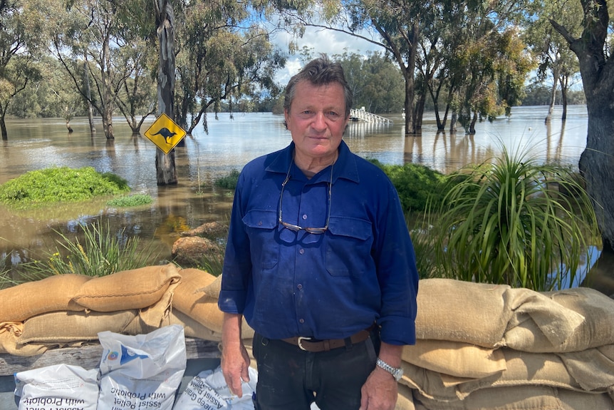  A middle aged man standing in front of some sandbags and flood water