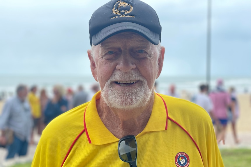 A man in a yellow and red surf life saving uniform smiles at the camera 