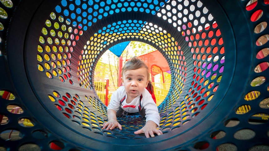 Young boy climbs through a tunnel in a children's playground.