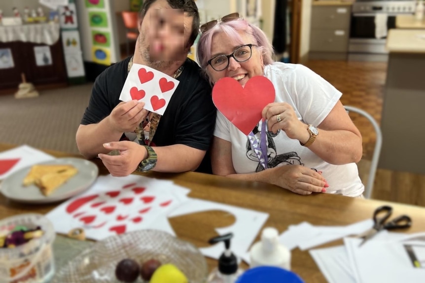 Disability worker with client smiling holding art work.