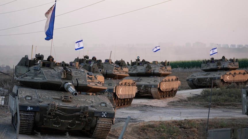 Four Israeli tanks drive in a line, with small Israeli flags flying from them.