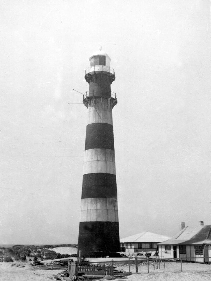 Black and white image of a tall striped light house with beach sand