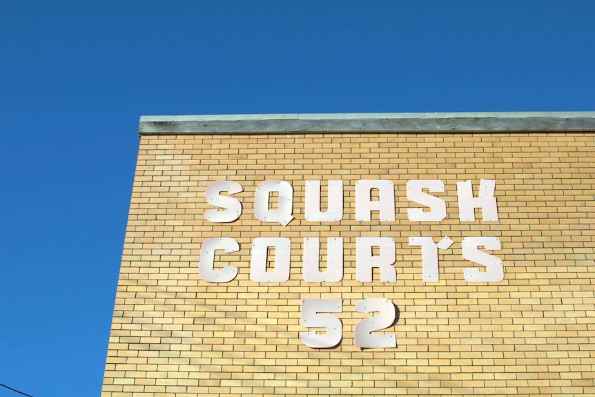Yellow brick wall against a blue sky with metal letters spelling out Squash Courts 52