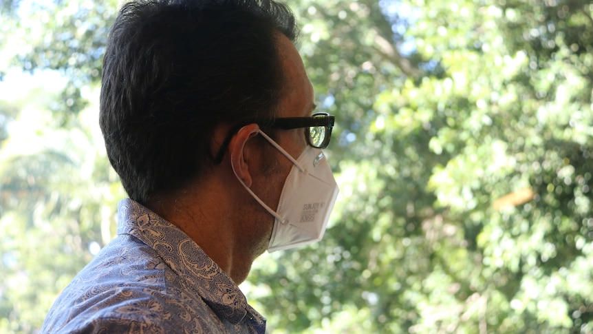 A man in a face mask stares out a window