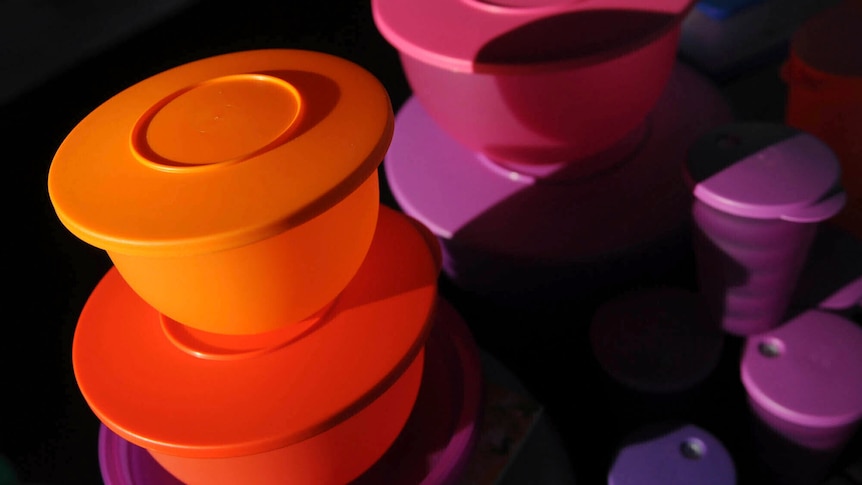 An image of orange, pink and purple round Tupperware boxes in a dark space.