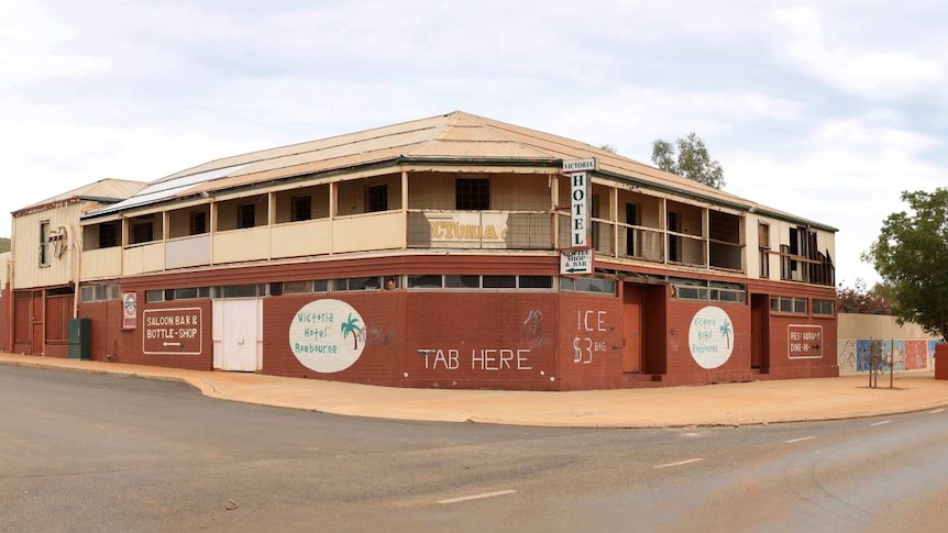An old-looking hotel with a large wall out the front. On the second-storey verandah, there is a broken sign.