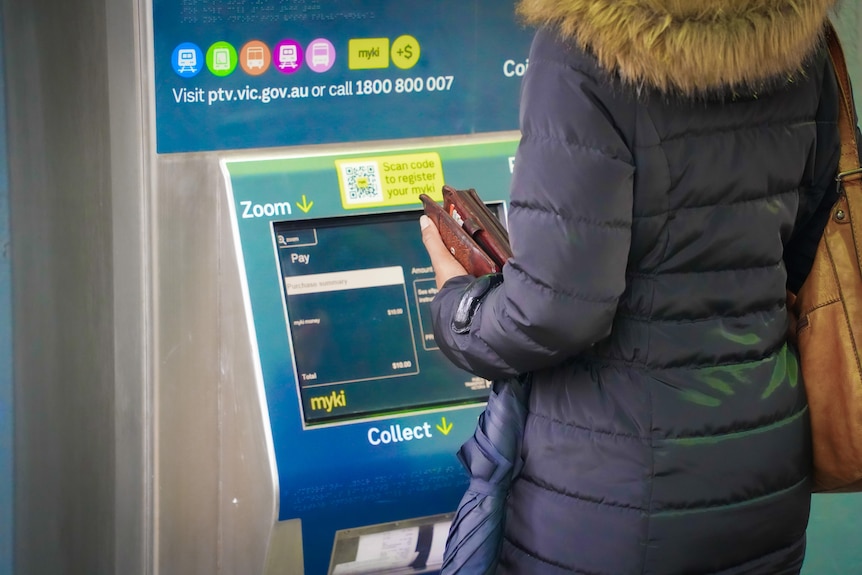 A woman wearing a puffer jacket uses a myki ticket machine.