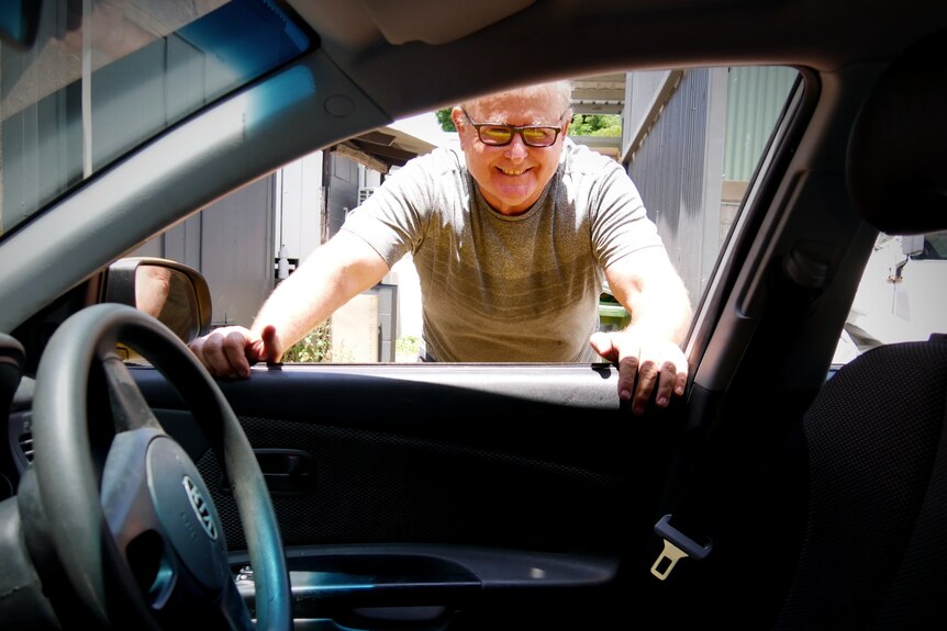 A man in his mid-50s looks into a car from the driver-side window.