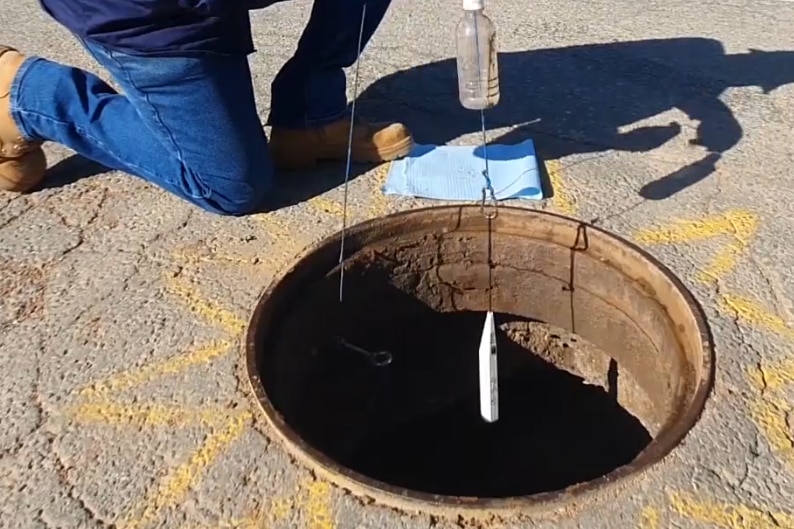 hands lower a small torpedo shaped device into a drain