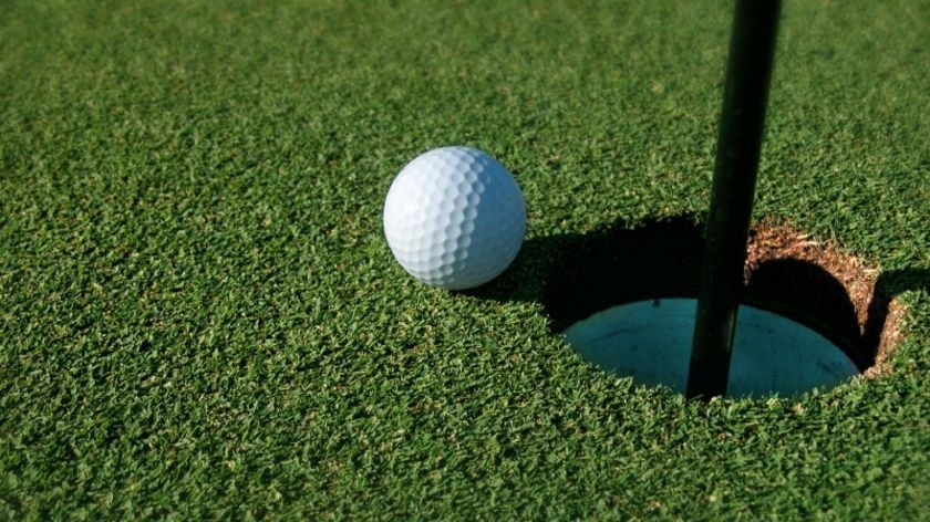 Golf ball on green sits on the edge of a hole.