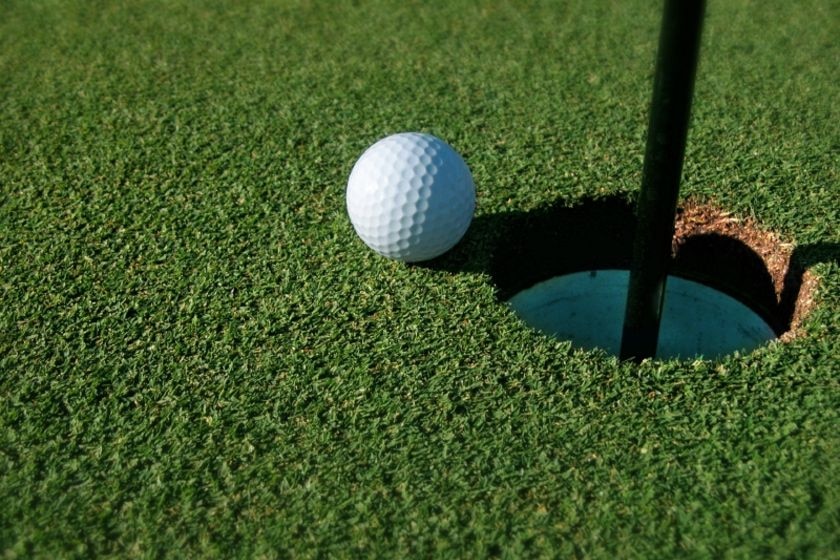 Golf ball on green sits on the edge of a hole.