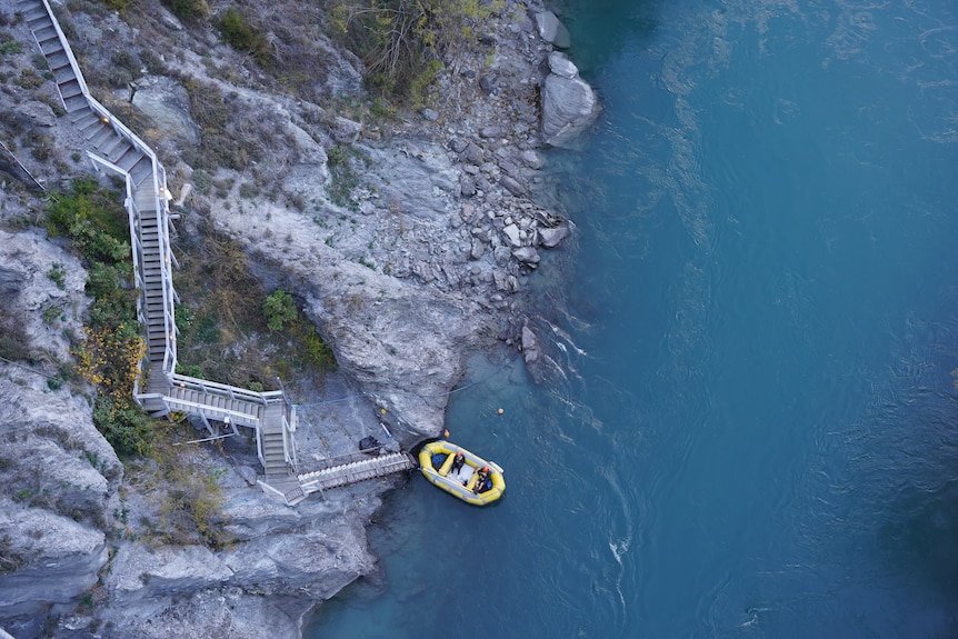 A photo from above of an inflatable yellow raft docking at river in New Zealand. 