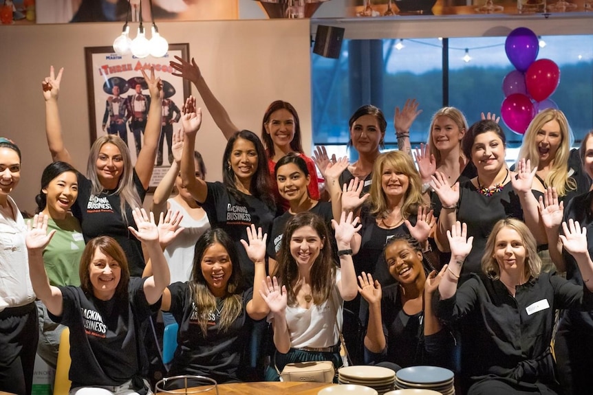 A group of women raise their hands and smile.