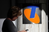 A woman checks her mobile phone near a Telstra sign