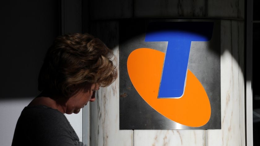 A woman checks her mobile phone as she walks past Telstra signage