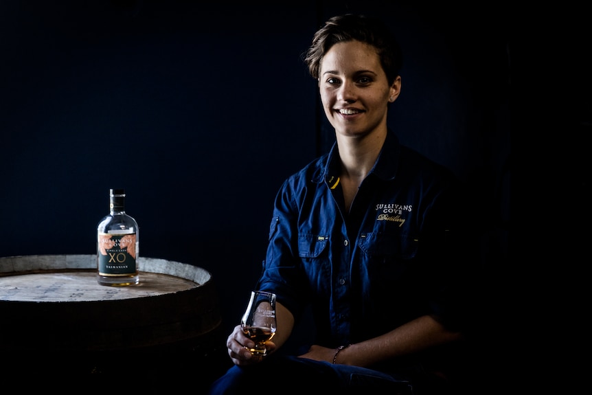 woman wearing blue shirt with a bottle of whiskey on a barrel