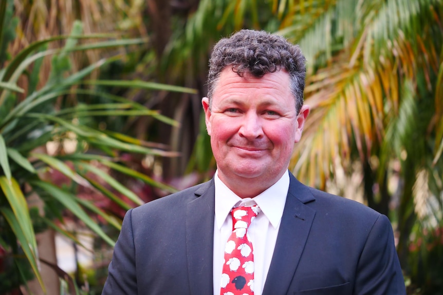 A man with a sheep tie stands in front of a plant