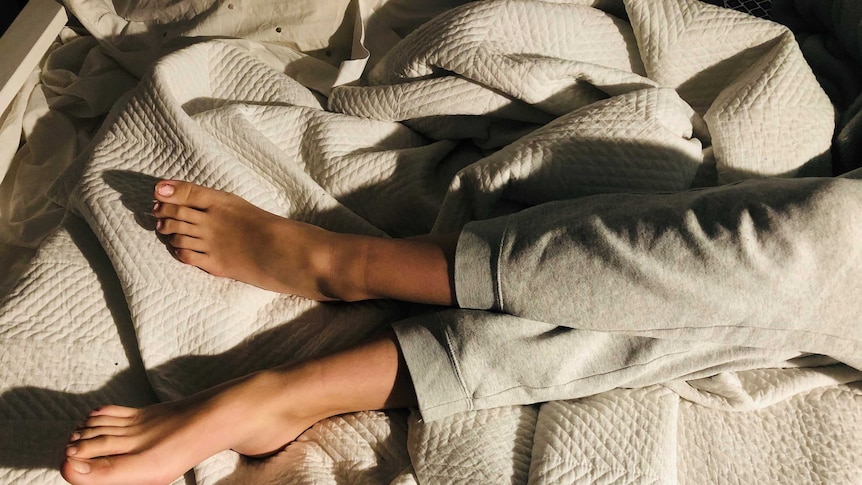Girls legs in grey merle sweat pants crossed in crumpled bedding