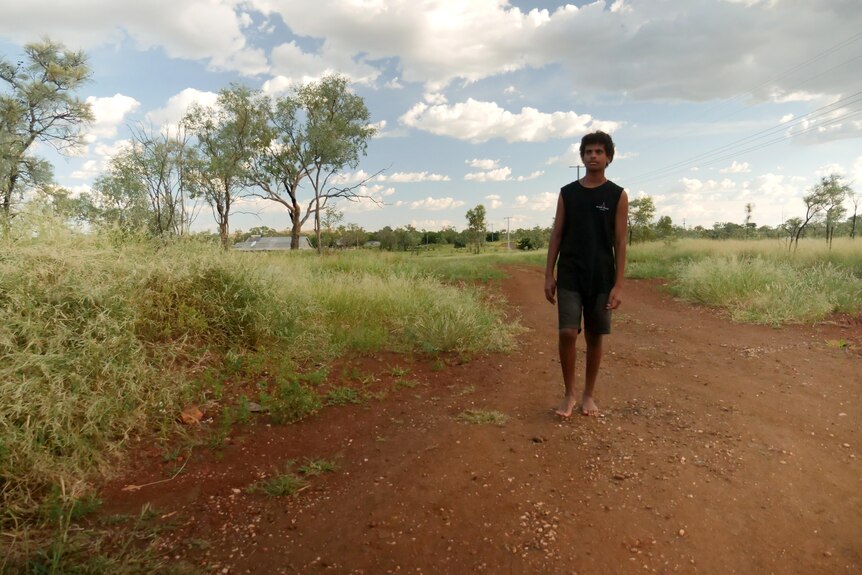 A boy in a black singlet and shorts walks barefoot along a dirt path
