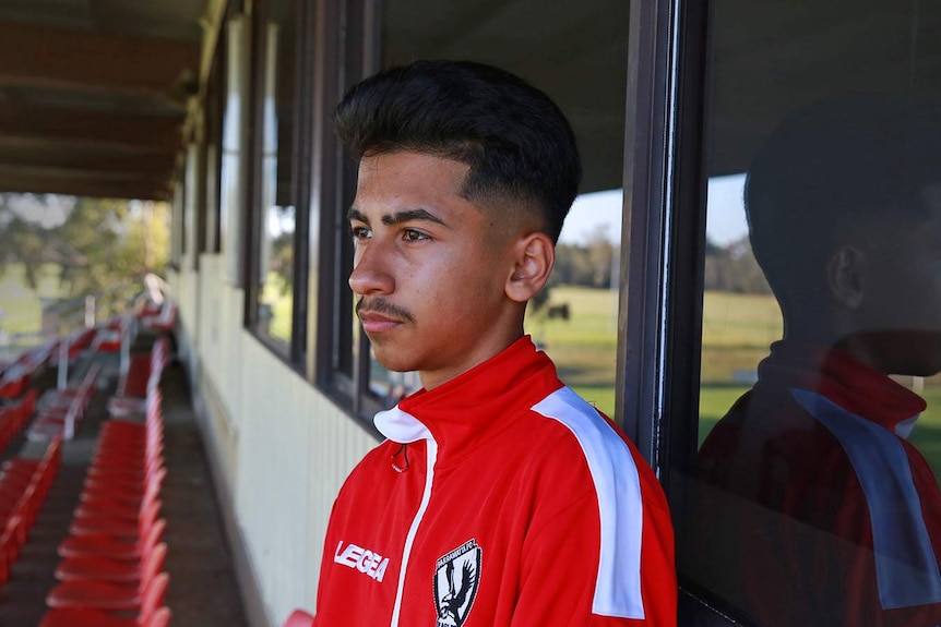 Teenage boy looks out across the field from his home stands.