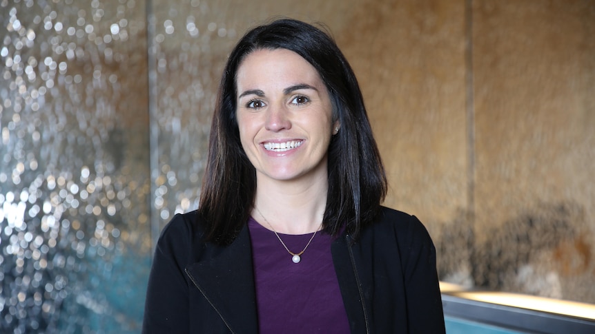 Kate Fitz-Gibbon looking straight at the camera and smiling, wearing a black jacket