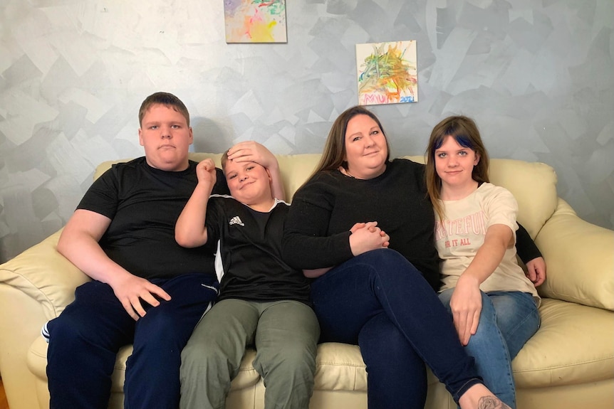 A mother sits with her three children on a couch. 