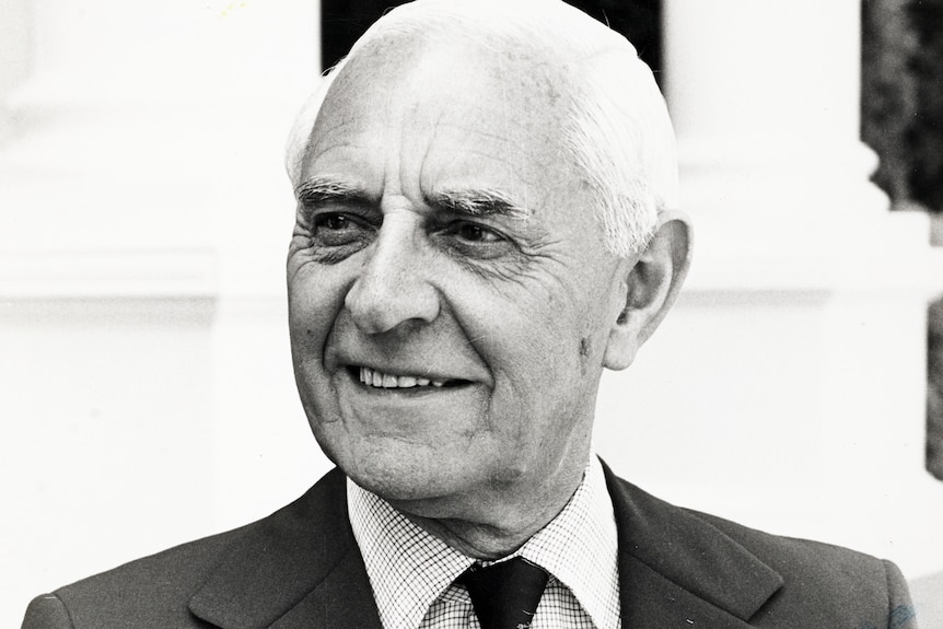 A black-and-white photo of a grey-haired man wearing a suit and smiling.