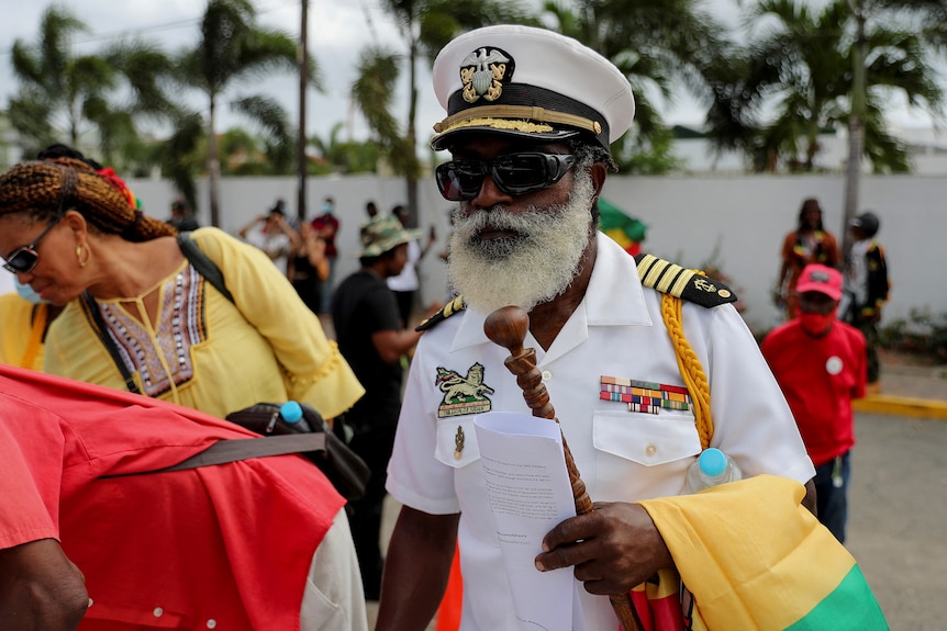 A man wearing a uniform carrying a jamaican flag and a letter at a protest on the streets