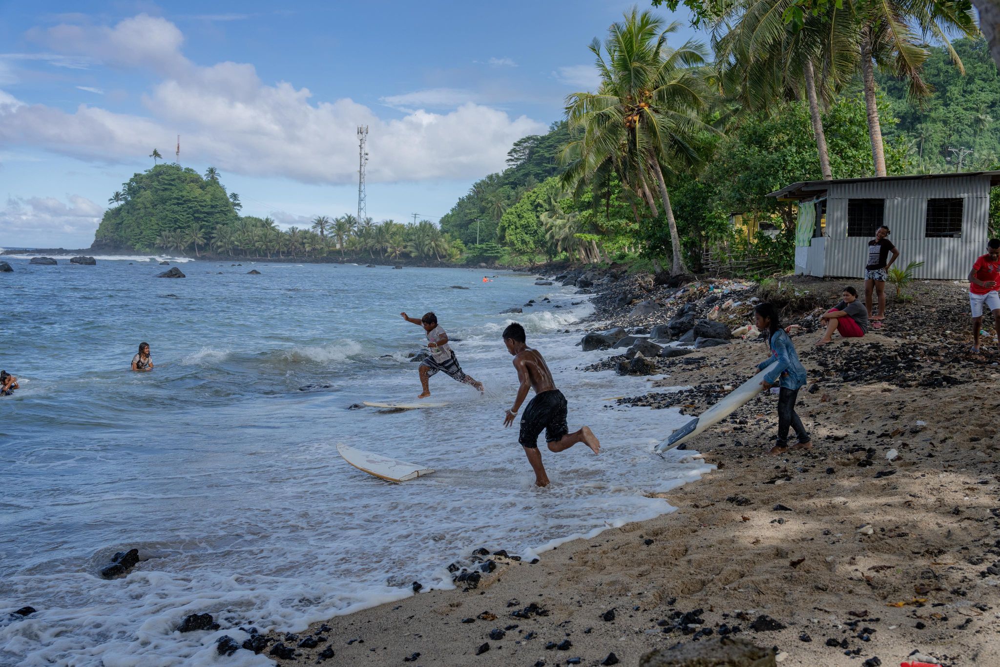 Samoan village kids running in the shallow surf to get their broken half board, playing in the water.