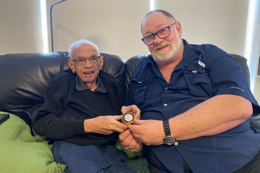 Two men sitting on a sofa holding a war medal