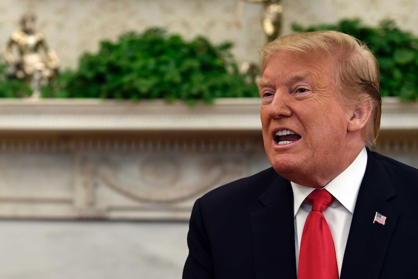 Donald Trump has his mouth open while speaking, and is wearing an American flag pin on his lapel.