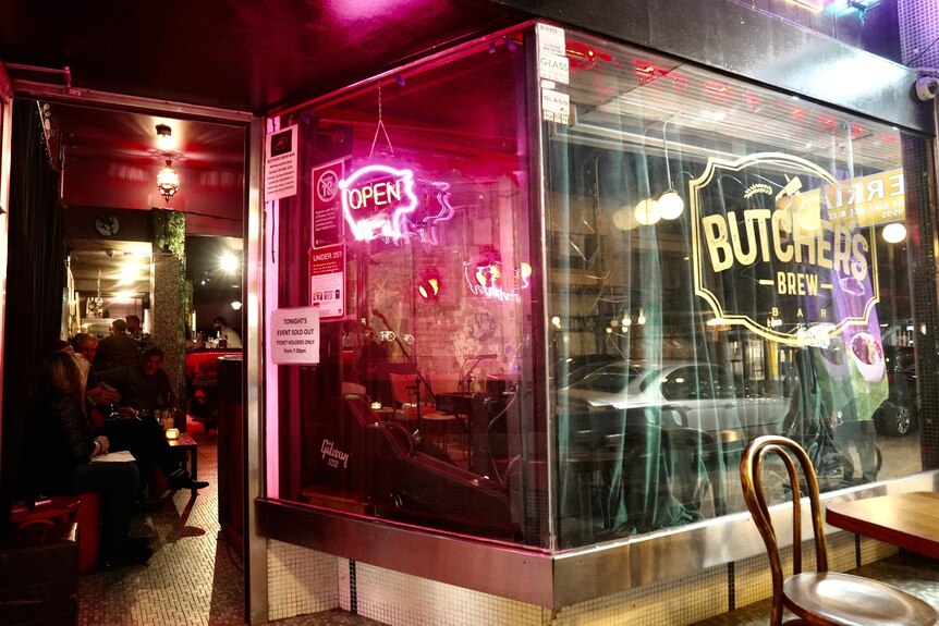 A neon "open" sign is illuminated at the entry of the Butchers Brew small bar