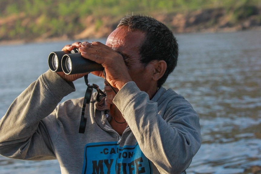 A man looks through a pair of binoculars.