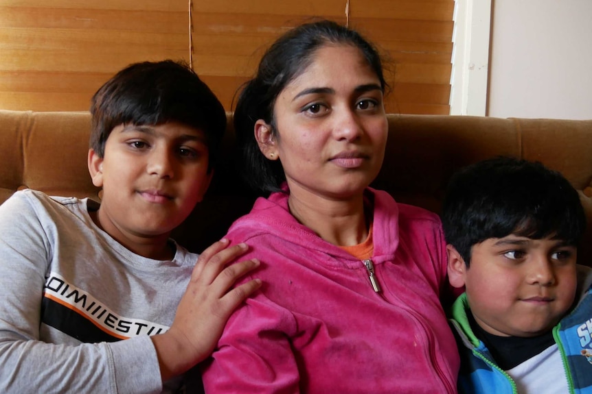 A migrant woman seated on a couch with her two sons who are aged 10 and 7.