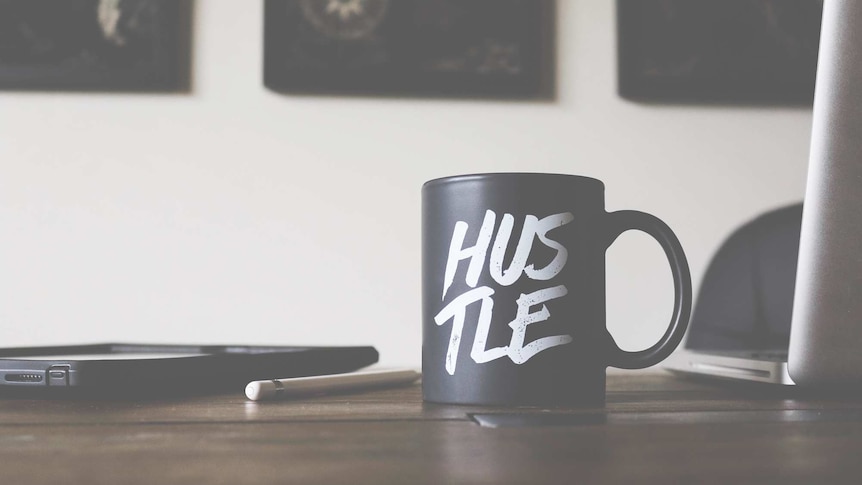 Coffee mug sitting on an office desk with the word hustle.