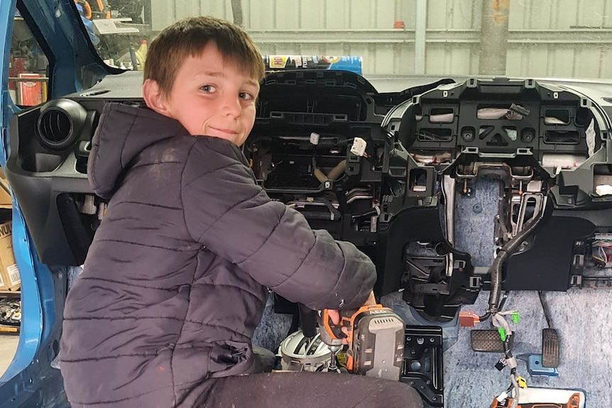 A boy uses tools to dismantle a vehicle.